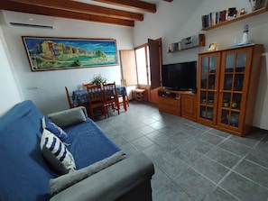 A living room with a sofa, TV, wooden cabinet, dining table, chairs, and a painting on the wall.