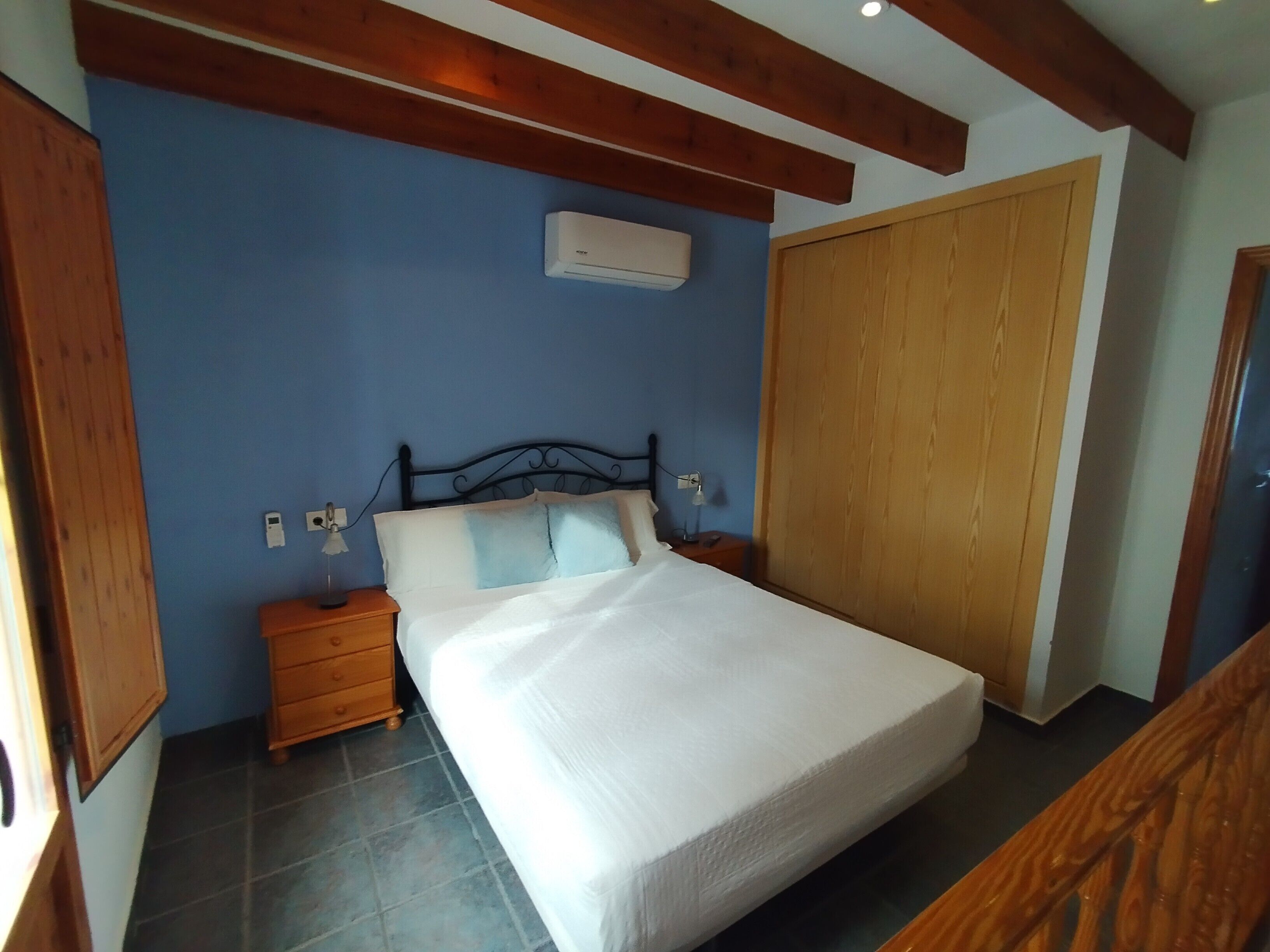Un dormitorio con cama, cabecero de madera, mesitas de noche, aire acondicionado y armario.