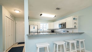 A kitchen with white cabinets, a microwave, a refrigerator, and a bar area with stools.