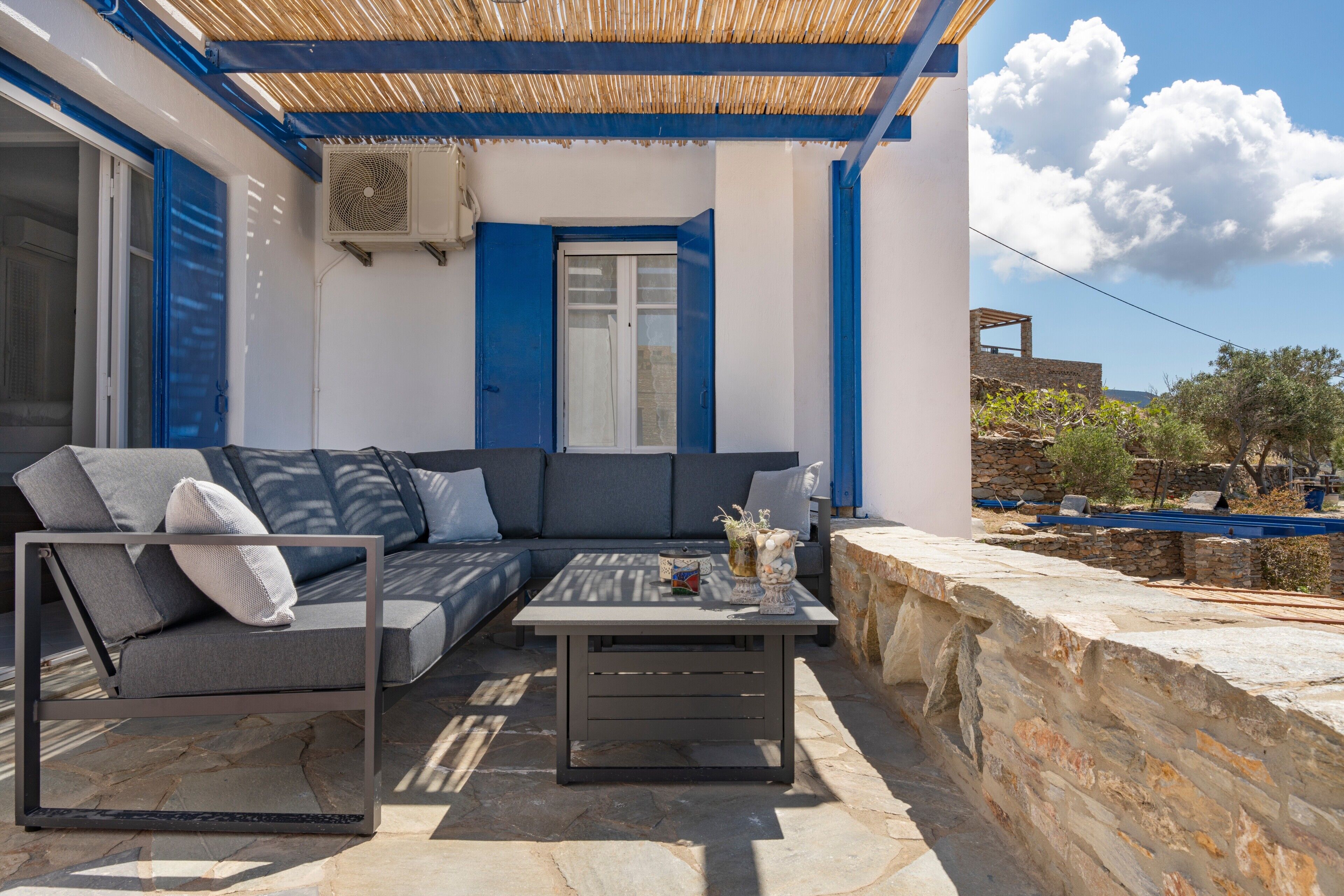 An outdoor seating area with a sofa and a table, a stone wall, and a building in the background.