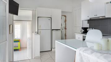 A kitchen with white cabinets, a refrigerator, a glass table with candles, and a view into a room with a bed and a window.