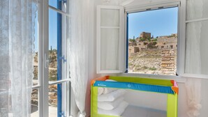 A room with a window, a baby crib, and a view of ancient ruins.