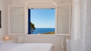 A bedroom with a bed, a window with open shutters, and a view of the sea.