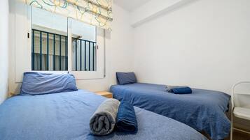 Una habitación con dos camas, una ventana con cortina, una silla y una mesita.