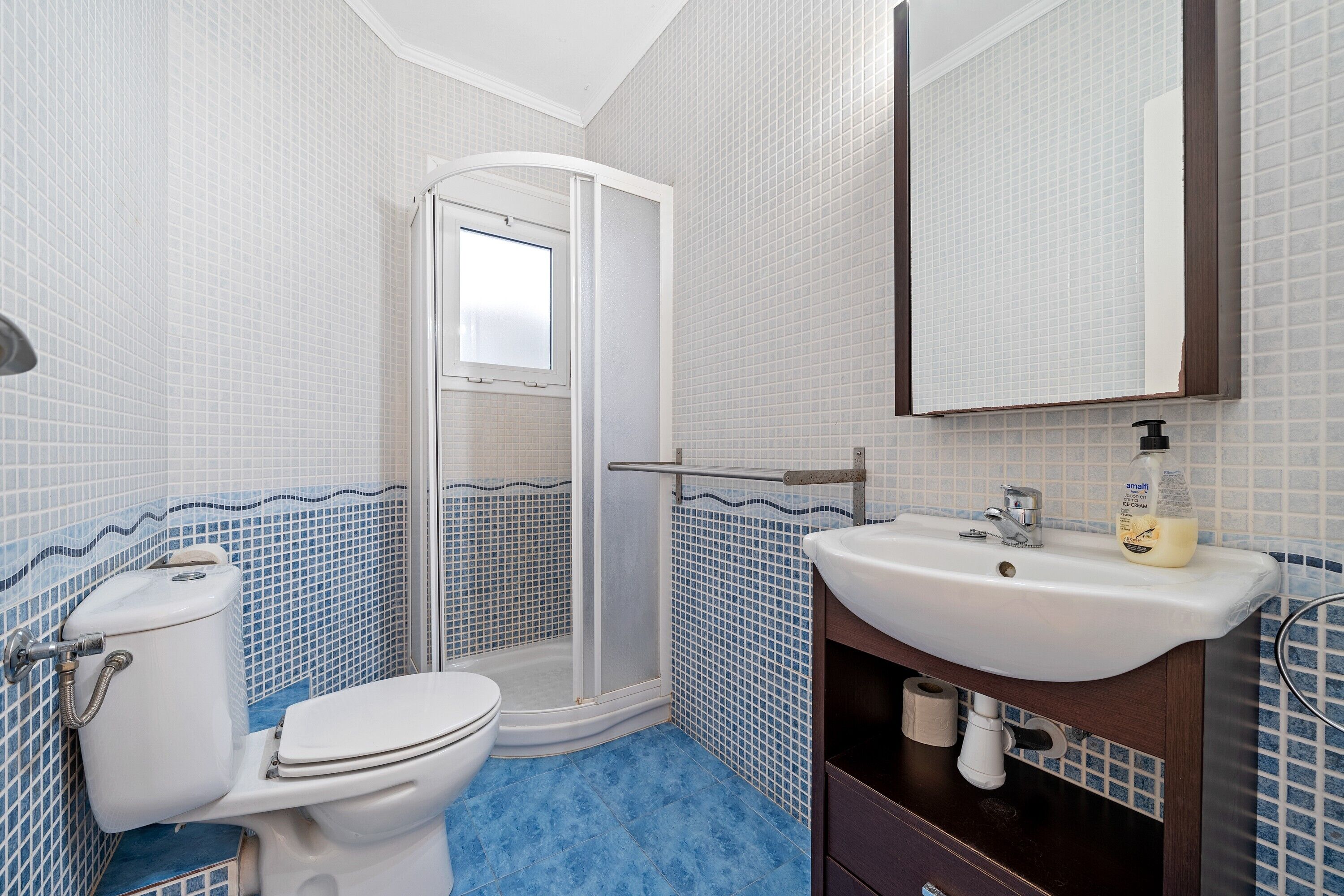 Un baño con inodoro, ducha, lavabo y espejo.