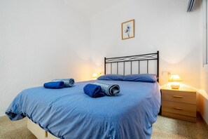 A neatly made bed with blue bedding, a bedside lamp, and a wooden nightstand. - Apartment 'Vista Mar' with Sea View, Wi-Fi and Air Conditioning (l'ampolla)