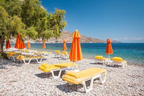 En strand med solstolar och parasoller, en stenstrand och ett klart, blått hav.