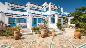 Un bâtiment blanc agrémenté de touches de bleu, de jardinières en terre cuite et d’une terrasse carrelée.