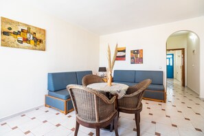 A room with a blue sofa, wicker chairs, a small table, and a painting on the wall. - Holiday Home 'Livadia Beach Suite ' with Sea View, Wi-Fi and Air Conditioning (tilos)