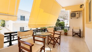 A balcony with yellow awnings, wooden chairs, a small round table, and a potted plant. - Holiday Home 'Olympus Tilos Apt Twin A3 ' with Mountain View, Wi-Fi and Air Conditioning (Tilos)