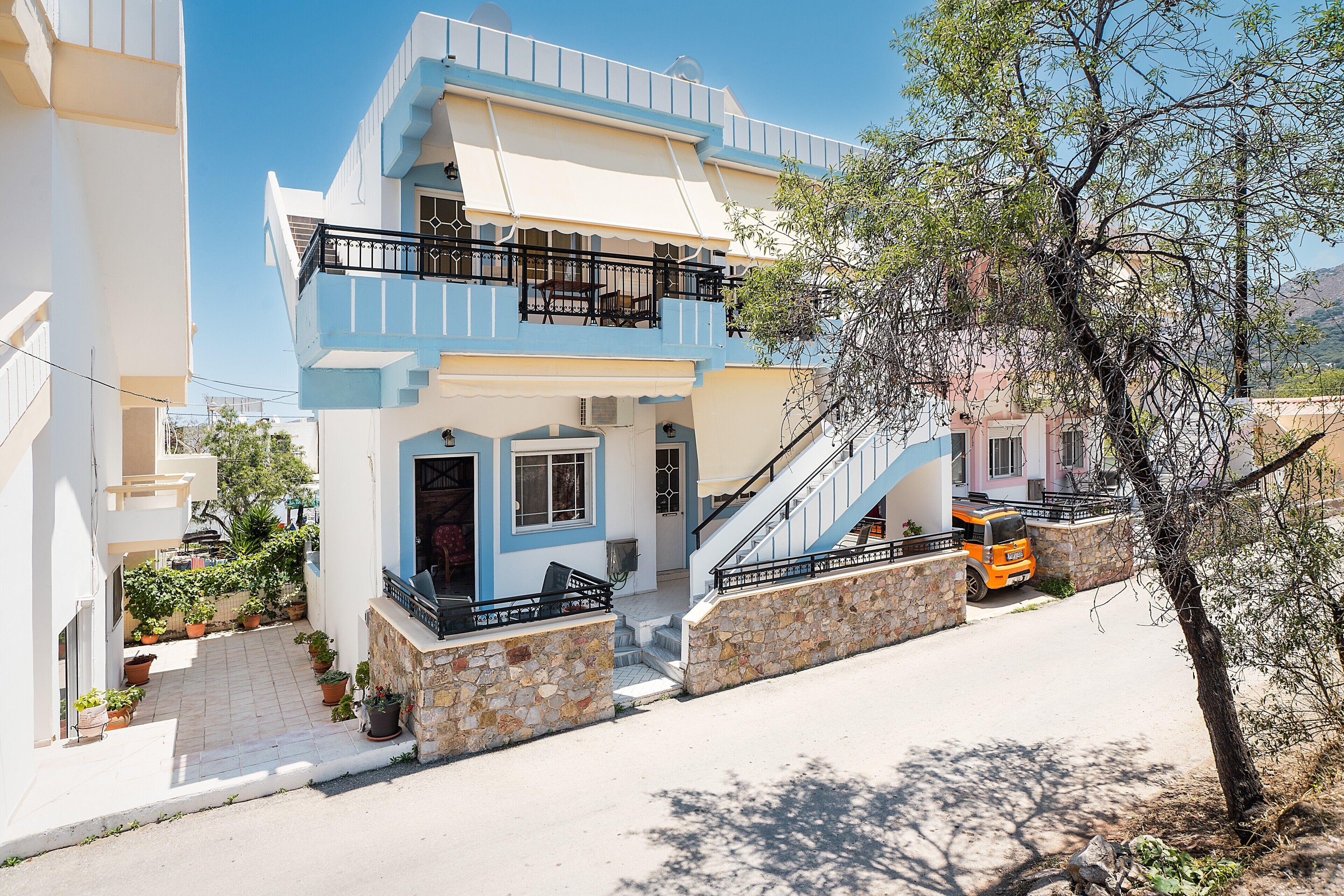 Um edifício de dois andares com varanda, escadaria e um veículo estacionado.