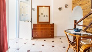 Ein Zimmer mit einem Holzkapständer, einem Glastisch mit einer blauen Schüssel, einem Holzstuhl, einer Tür mit Glassfeldern und einem Fliesenboden.
