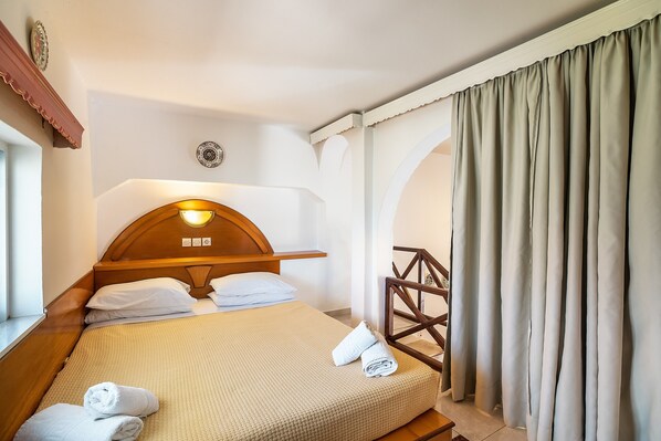 Une chambre d’hôtel avec une tête de lit en bois, un lit avec du linge de maison blanc, une table de chevet et une fenêtre avec des rideaux.