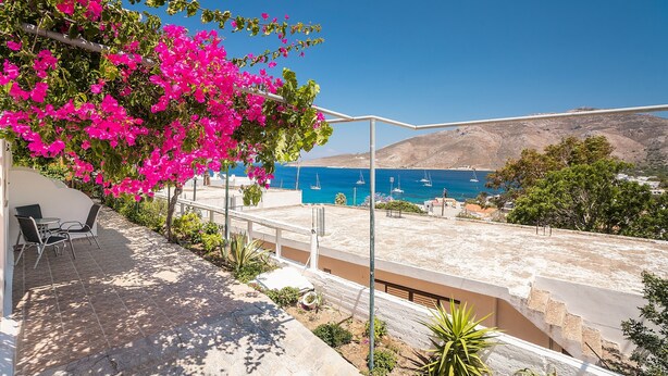 A rooftop terrace with a view of the sea, outdoor furniture, and a pergola with flowering plants.