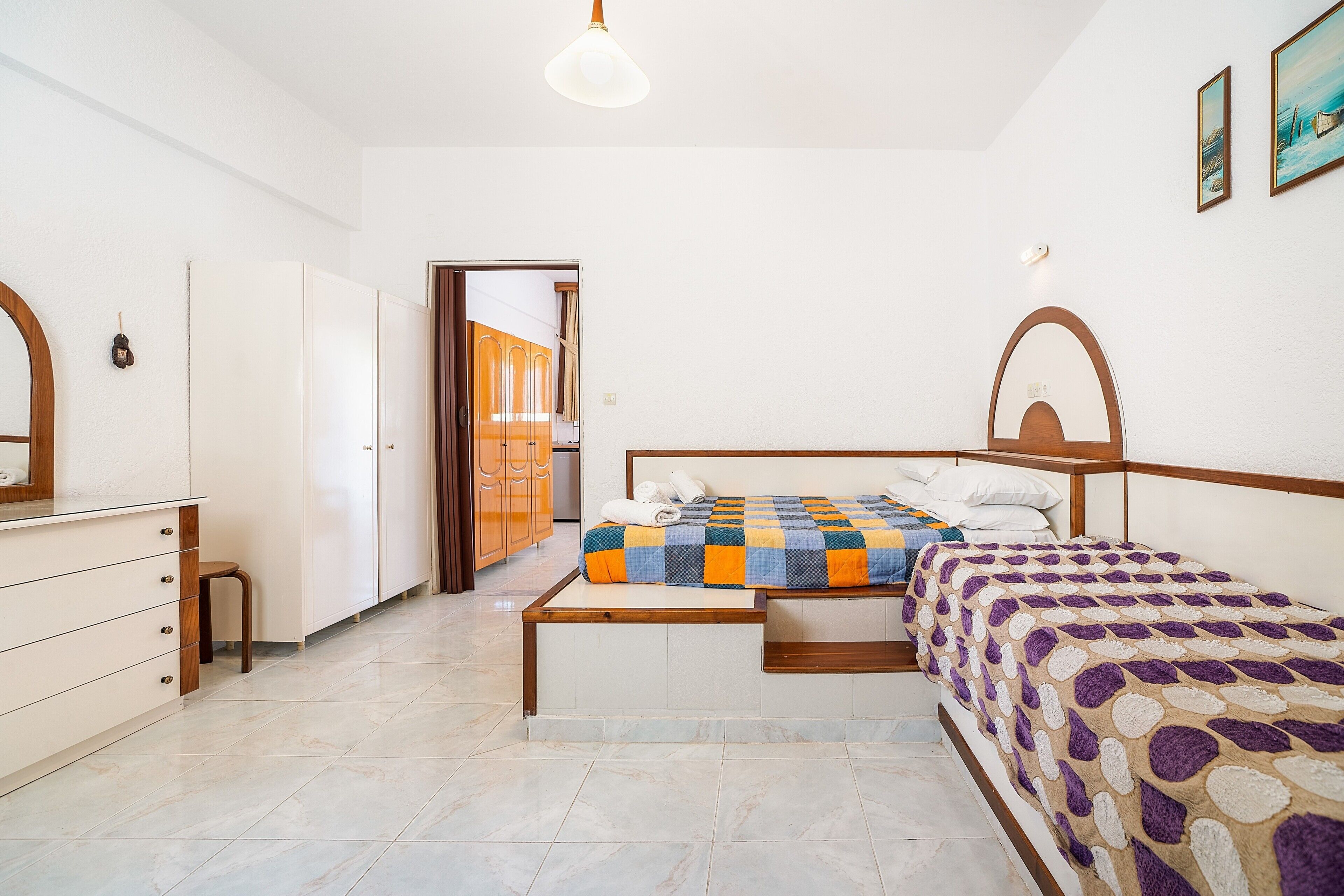 Une chambre à coucher comprenant un lit, une commode, un miroir et une porte donnant sur une autre pièce.