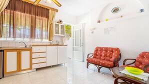 A kitchen with a sink, cabinets, and a window with curtains. There is a dining area with a table and chairs.