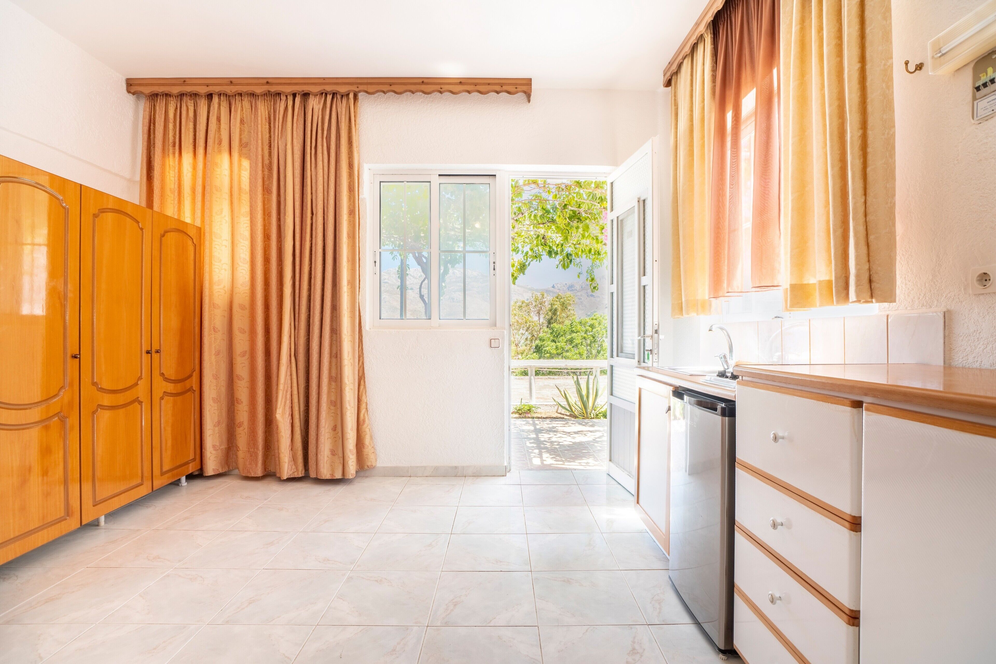 A kitchen with wooden cabinets, a dishwasher, and a window with curtains.