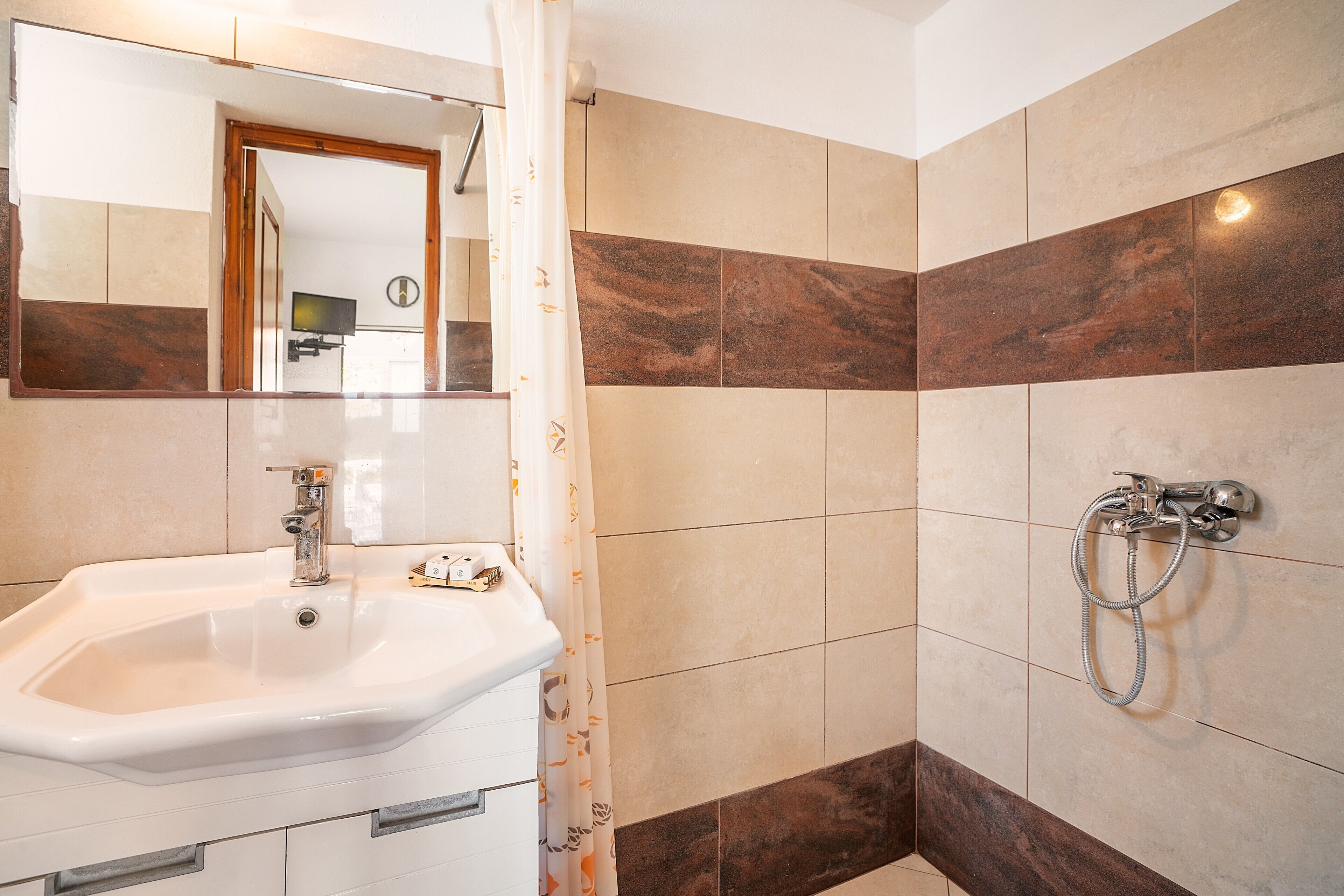 Ein Badezimmer mit Waschbecken, Spiegel, Dusche und gefliesten Wänden.