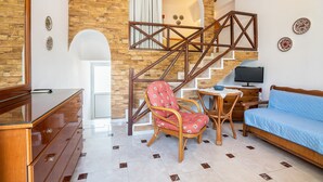 Una habitación con una escalera de madera, un sofá, una silla, un televisor y un aparador de madera.