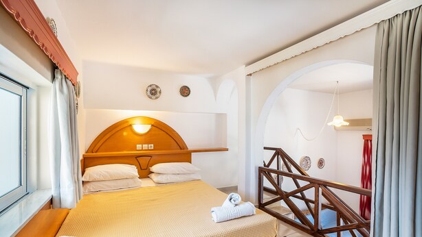 Habitación de hotel con cama, cabecero de madera, una escalera y vistas al exterior.