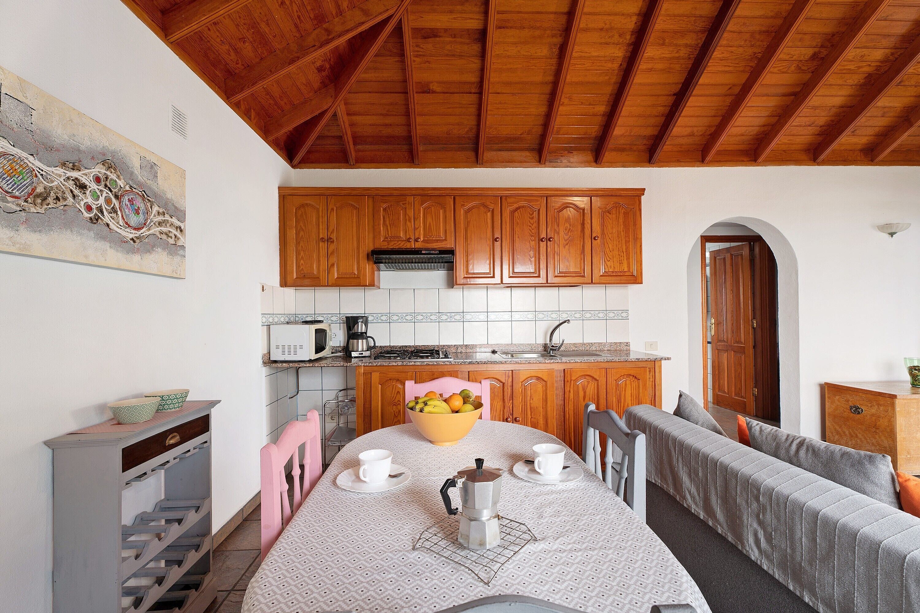 Una cucina con mobili in legno, un tavolo da pranzo con una caffettiera e una ciotola di frutta.
