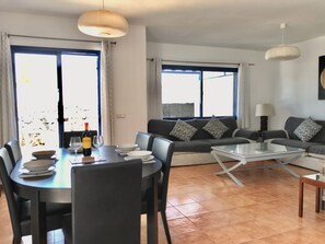 Uma sala de estar moderna com área de jantar, com um conjunto de sofá, uma mesa de centro de vidro e uma mesa de jantar com cadeiras.