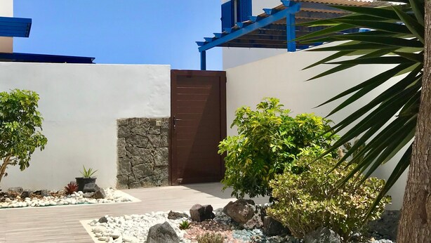 A modern building with a stone wall, a wooden door, and a pathway leading to a gate. - Holiday Home 'Villa Katarina' with Private Pool, Wi-Fi and Air Conditioning (Lanzarote)