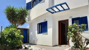A modern building with white walls and blue shutters, a wooden door, and a garden with white pebbles and plants. - Holiday Home 'Villa Katarina' with Private Pool, Wi-Fi and Air Conditioning (Lanzarote)
