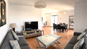A living room with a TV, sofa, coffee table, dining area with chairs, and a bookshelf. - Holiday Home 'Villa Katarina' with Private Pool, Wi-Fi and Air Conditioning (Lanzarote)