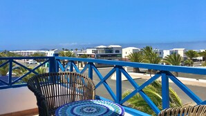 A balcony with a view of a coastal town, a wicker chair, and a patterned table. - Holiday Home 'Villa Katarina' with Private Pool, Wi-Fi and Air Conditioning (Lanzarote)