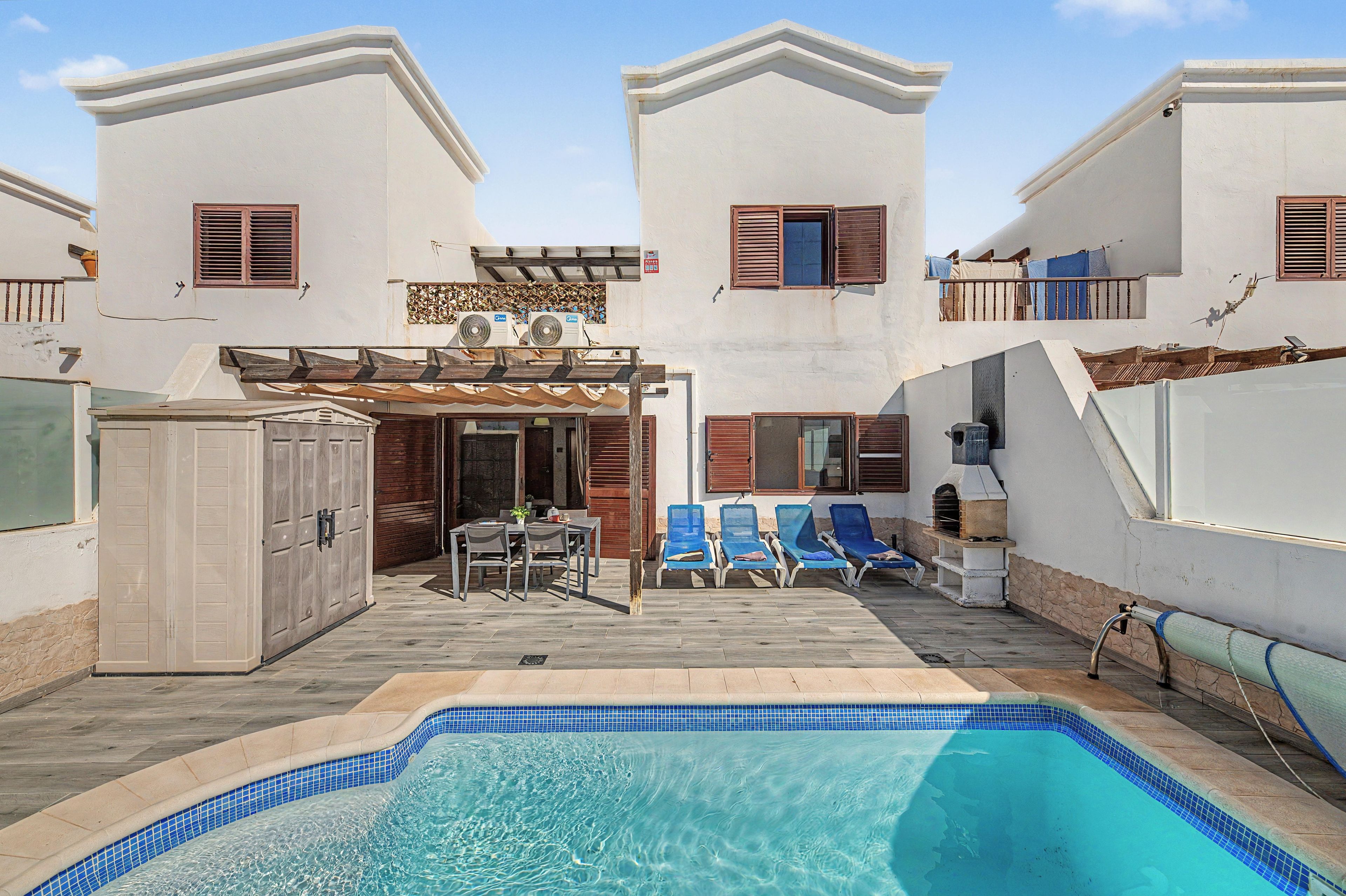 A pool area with a clear blue pool, lounge chairs, and a covered seating area with a table and chairs.