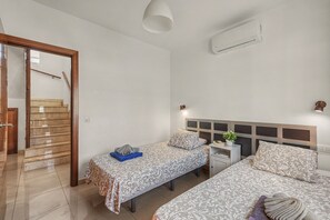 A hotel room with two beds, a small table, a nightstand, a wall-mounted air conditioner, and a staircase leading to another room.