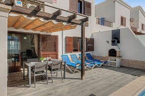 Un espace extérieur abrité, avec une table et des chaises, un barbecue et des fauteuils de jardin bleus.