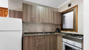 Une cuisine compacte avec des meubles en bois, une cuisinière à gaz encastrée, un évier et un réfrigérateur blanc.
