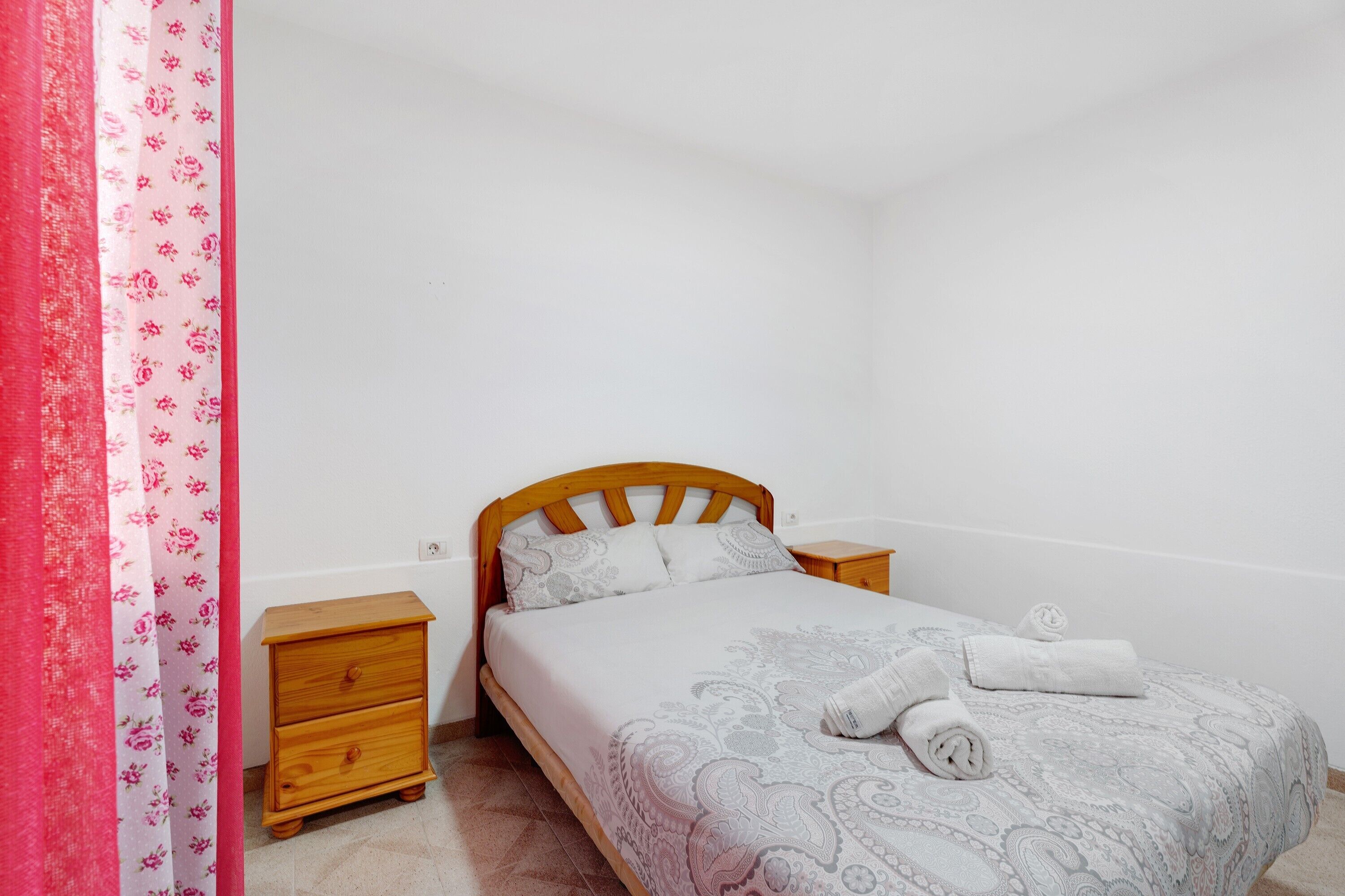 Ein Schlafzimmer mit einem hölzernen Bett, einem Nachttisch, einer kleinen Kommode und einem zusammengerollten Handtuch auf dem Bett.
