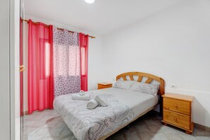Une chambre à coucher avec un lit, une table de chevet en bois et une fenêtre avec des rideaux rouges.