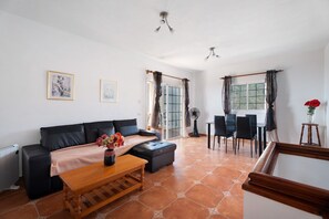 A living room with a sofa, ottoman, coffee table, and a dining area with chairs and a table.