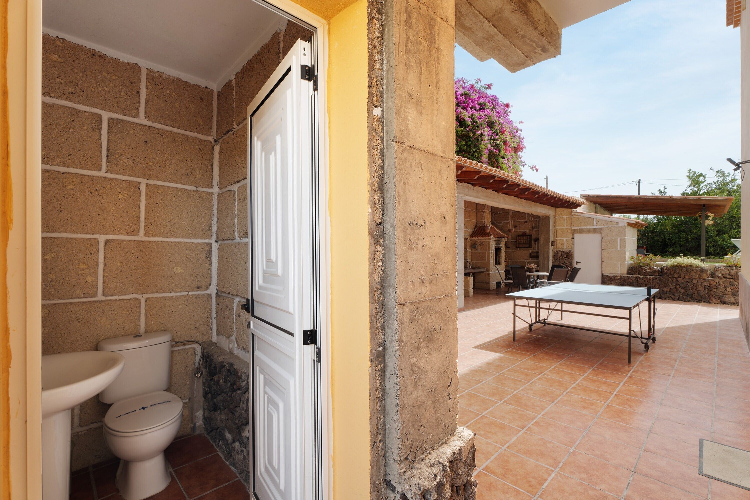 A bathroom with a toilet and sink, a door leading to an outdoor patio with a table and chairs.
