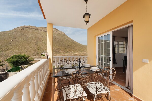 A balcony with a table set for dining, a hanging light fixture, and a view of a mountain.