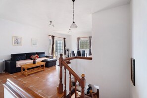 A spacious living area with a wooden staircase, a sofa, a coffee table, and a dining table with chairs.