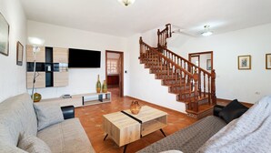 Amplia sala de estar con escalera de madera, televisor de pantalla plana y sofá.