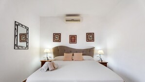 Una cama bien hecha con cabecera, dos lámparas de noche y un aire acondicionado de pared.