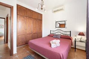A bedroom with a bed, wooden wardrobe, mirror, lamp, and a small table.