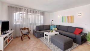 A modern living room with a grey sofa, a white coffee table, a TV, and a decorative chair.