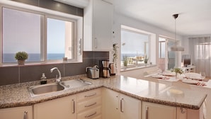 A modern kitchen with granite countertops, stainless steel appliances, and a large window overlooking the sea.