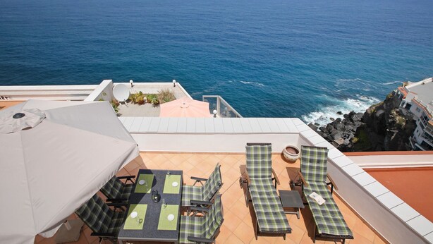 A terrace with a table and chairs, a sun umbrella, and a view of the ocean.
