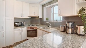 A modern kitchen with white cabinets, a granite countertop, a built-in oven, a coffee maker, and a kettle.