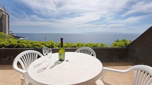 Een ronde tafel met twee stoelen, een fles wijn en twee wijnglazen op een terras met uitzicht op zee.