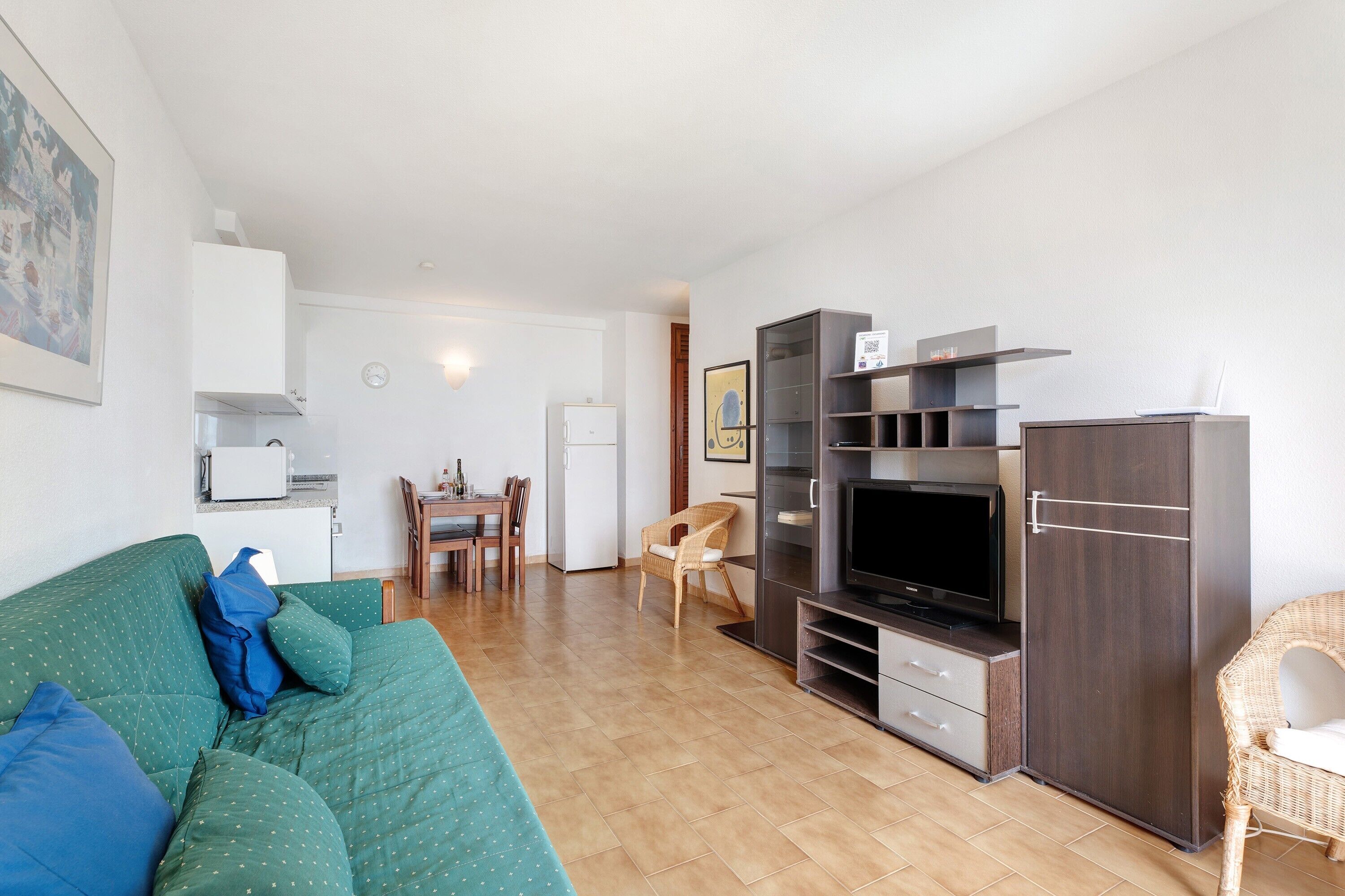 Een zithoek met een bank, televisie, entertainmentkast, eettafel, stoelen en een keuken.