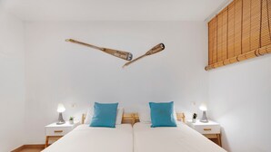 Een tweepersoonsbed met witte beddengoed, twee blauwe kussens, twee nachtkastjes met lampen en een houten vloer.